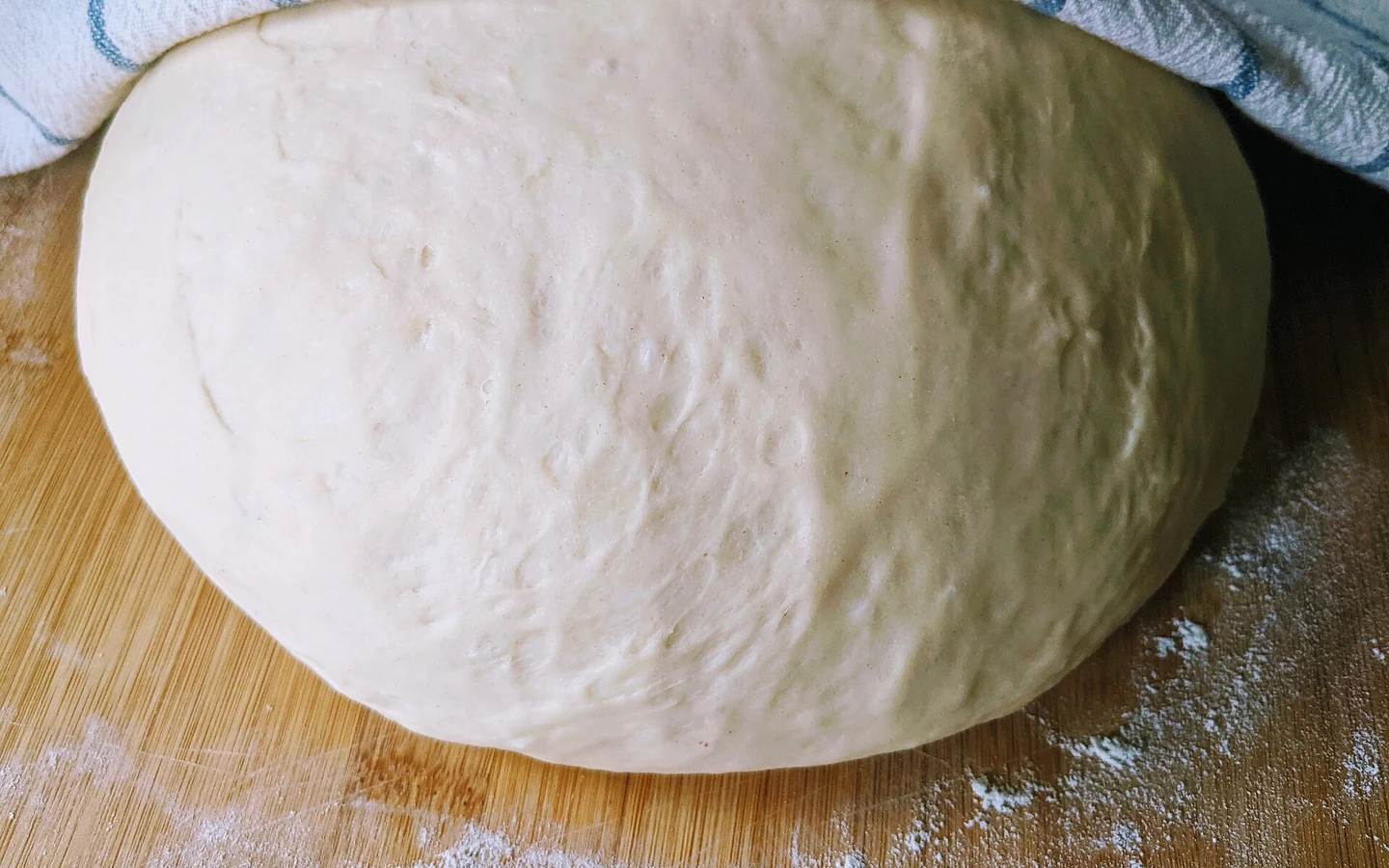 Bread dough rests on a floured work surface under a partly folded cloth.
