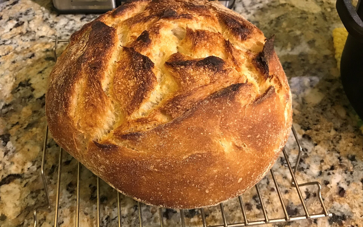 A sourdough loaf with a deeply browned, scored crust cools after baking.