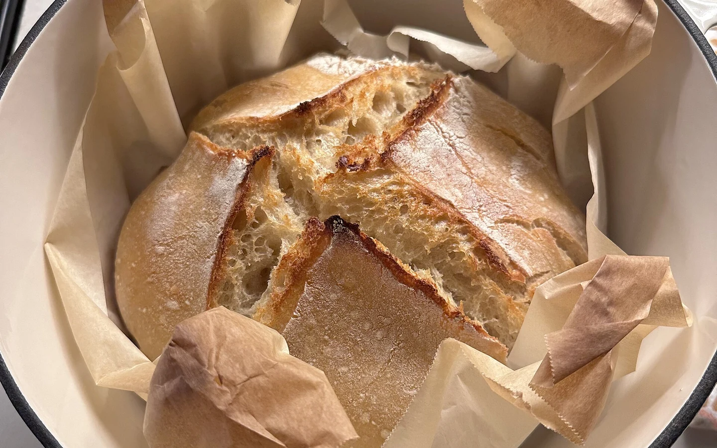 A homemade sourdough boule rests on parchment inside an open cast-iron pot.