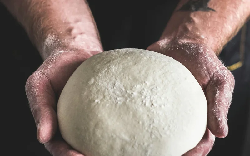 A baker stretches a sheet of dough between both hands.