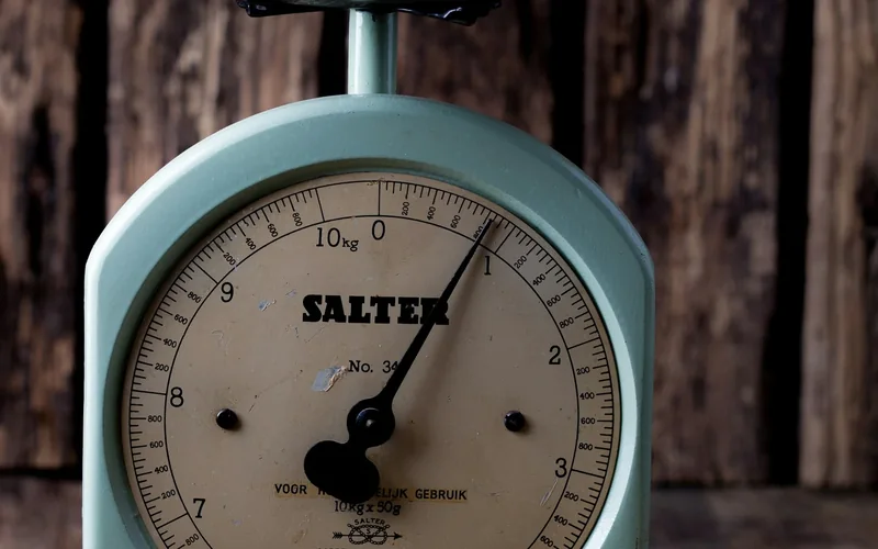 A blue kitchen scale with a round dial and metal weighing bowl.