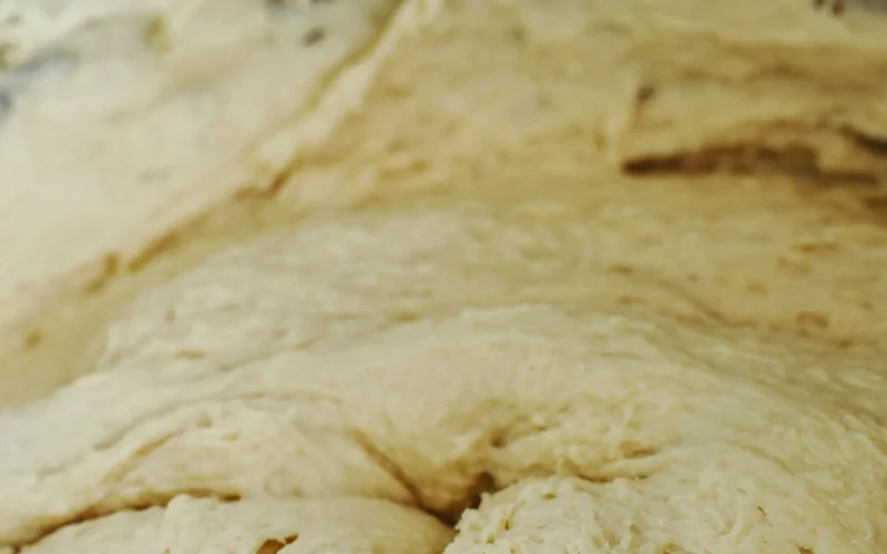 Wet bread dough is being mixed in a bowl.