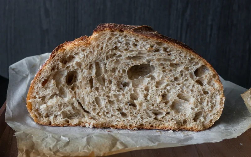 A baked sourdough loaf shows an opened score across its crust.