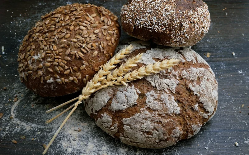 Three rustic loaves are arranged with wheat stalks on a wooden table.
