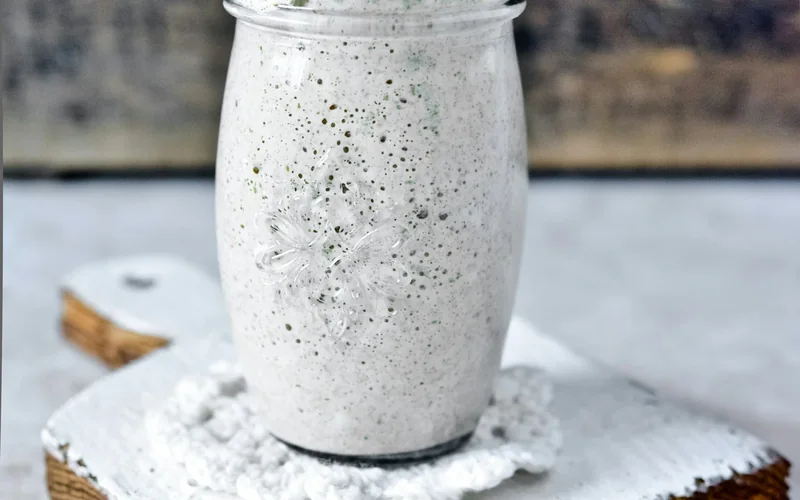 A glass jar of sourdough starter stands on a light wooden surface.