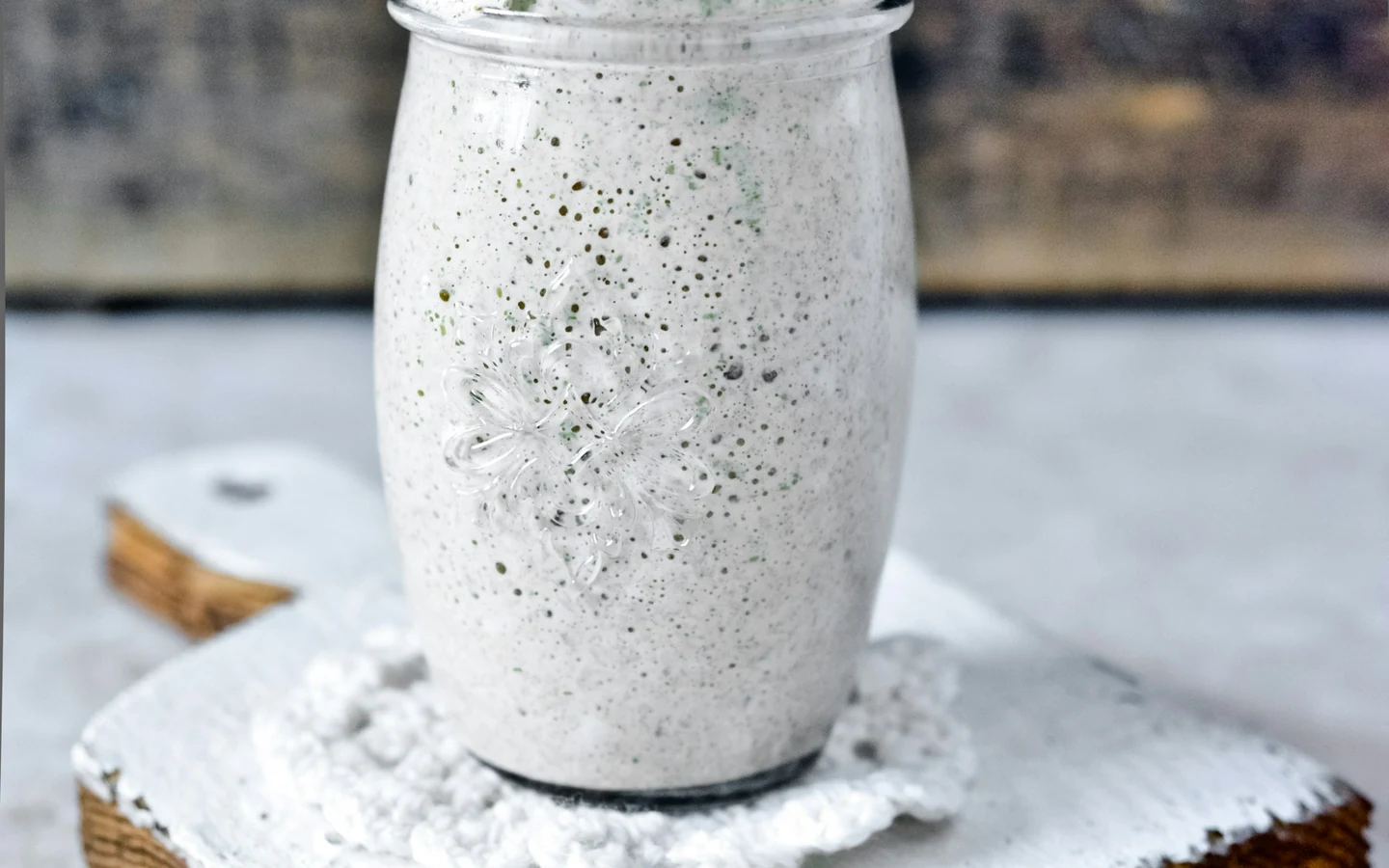 A glass jar of sourdough starter stands on a light wooden surface.