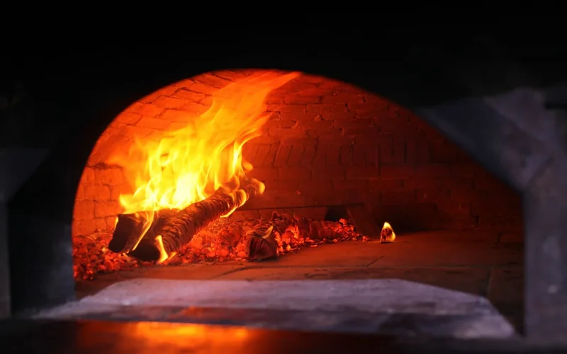 A wood fire burns inside a domed brick oven.